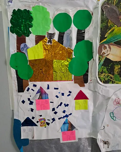 Detalle del mural: árboles de cartulina, casa de papel dorado con gato, casas de colores y papelitos azules