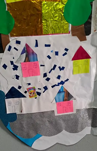 Detalle del mural: casas de cartulina, papelitos azules y la base de papel plateado (nubes)