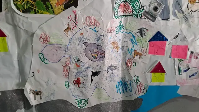 Detalle del mural: dibujo del mar o laguna con delfín, orca, tiburón y pulpo; casas de cartulina